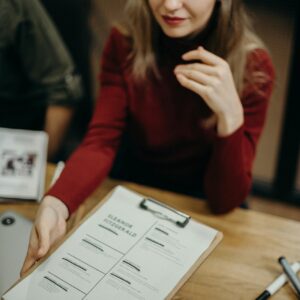 Woman sitting at a desk holding a clipboard and reviewing a resume during a job interview.